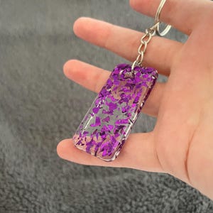 May include: A purple glitter keychain with a silver chain and ring. The glitter is embedded in clear resin.