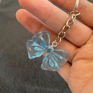 Puede incluir: Un llavero de plástico azul claro en forma de lazo con una cadena y un anillo plateados.