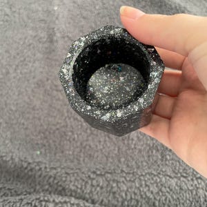 May include: A black octagonal planter with a glittery finish. The planter is made of resin and has a smooth, polished surface.