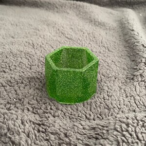 May include: A small, hexagonal green planter with a glittery finish. The planter is made of resin and is ideal for small plants or succulents.