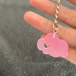 May include: A pink cloud-shaped keyring with a heart cutout. The keyring is attached to a silver chain and ring.