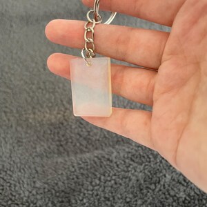 May include: A white rectangular keychain with a silver chain and ring. The keychain has a marbled pattern with shades of blue and white.