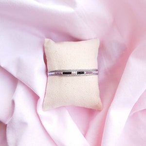 May include: A silver bracelet with black and pink beads on a white pillow.