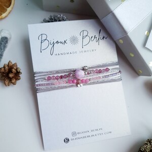 Puede incluir: Un conjunto de pulseras delicadas con cuentas rosas y plateadas, superpuestas en una tarjeta blanca con el texto "Bijoux Berlin Handmade Jewelry". La tarjeta también incluye los identificadores de redes sociales para Bijoux Berlin.