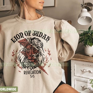 以下が含まれることがあります： ベージュ色のスウェットシャツ。ライオンの頭、稲妻、そして「LION OF JUDAH」と「REVELATION 5:5」の文字が描かれた、かすれたグラフィックが特徴です。デザインには赤と黒の要素が組み込まれています。スウェットシャツはニュートラルカラーです。
