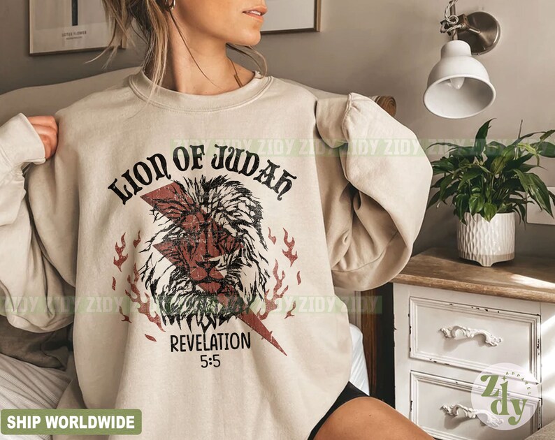 以下が含まれることがあります： ベージュ色のスウェットシャツ。ライオンの頭、稲妻、そして「LION OF JUDAH」と「REVELATION 5:5」の文字が描かれた、かすれたグラフィックが特徴です。デザインには赤と黒の要素が組み込まれています。スウェットシャツはニュートラルカラーです。