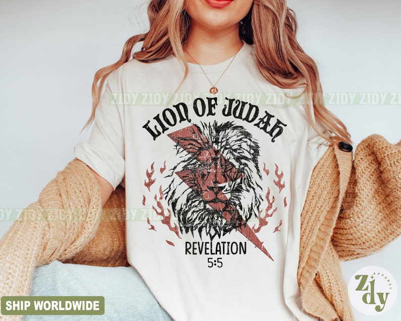 以下が含まれることがあります： クリーム色のTシャツ。 荒れたライオンの頭のグラフィック、稲妻、炎が特徴です。「LION OF JUDAH」と「REVELATION 5:5」の文字がプリントされています。 デザインは黒と赤です。 衣料品です。