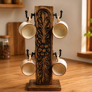 May include: A vertical wooden mug rack featuring a dark brown finish with a carved floral and leaf pattern on the front. The stand includes four black metal hooks, each holding a cream-colored ceramic mug with a simple handle and round rim.