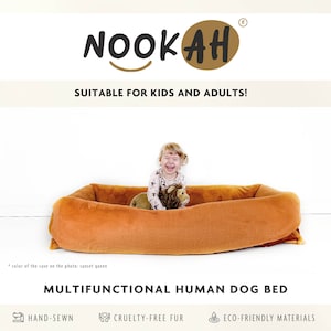 Puede incluir: Una cama para perros rectangular marrón con un niño sentado dentro. La cama está hecha de tela suave y de felpa y tiene un borde elevado. El niño sonríe y sostiene un animal de peluche. La cama está etiquetada como "CAMA MULTIFUNCIONAL PARA HUMANOS Y PERROS" y tiene iconos para "COSIDO A MANO", "PELO LIBRE DE CRUELDAD" y "MATERIALES ECOLÓGICOS".