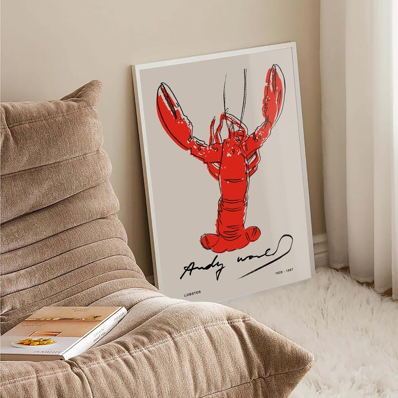 May include: A white framed print of a red lobster with black outlines. The artist's signature, "Andy Warhol", is written in black below the lobster. The text "Lobster" is written in black below the signature. The text "1928 - 1987" is written in black to the right of the signature.