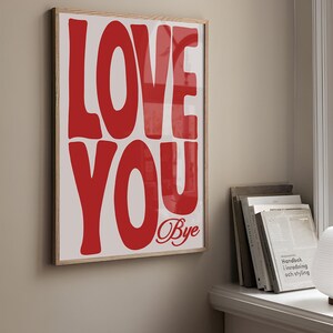 K&ouml;nnte beinhalten: Ein gerahmtes Poster mit den Worten "LOVE YOU" in gro&szlig;en, roten, fetten Buchstaben. Das Wort "Bye" ist darunter in Kursivschrift geschrieben.