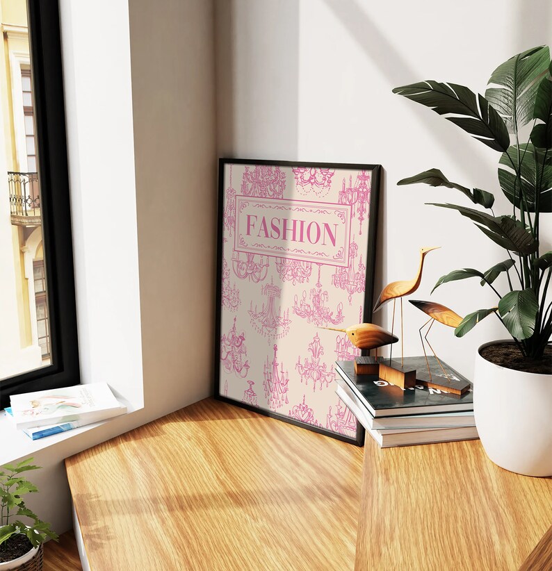 May include: A black framed print with a cream background and pink chandelier illustrations. The print has the word "FASHION" in a pink rectangle.