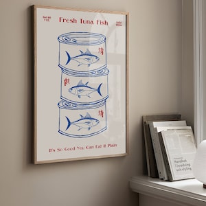 May include: A framed print featuring a stack of three blue and white tuna cans. The words "Fresh Tuna Fish" and "It's So Good You Can Eat It Plain" are printed in red. The net weight is 7 oz.