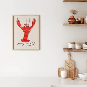 May include: A framed print of a red lobster with black outlines, the signature "Andy Warhol" and the text "Lobster 1962-1967" is displayed on a white wall.