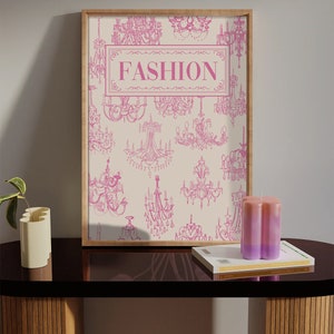 May include: A framed print with a white background and pink illustrations of chandeliers. The print has the word "FASHION" in pink letters in the centre.