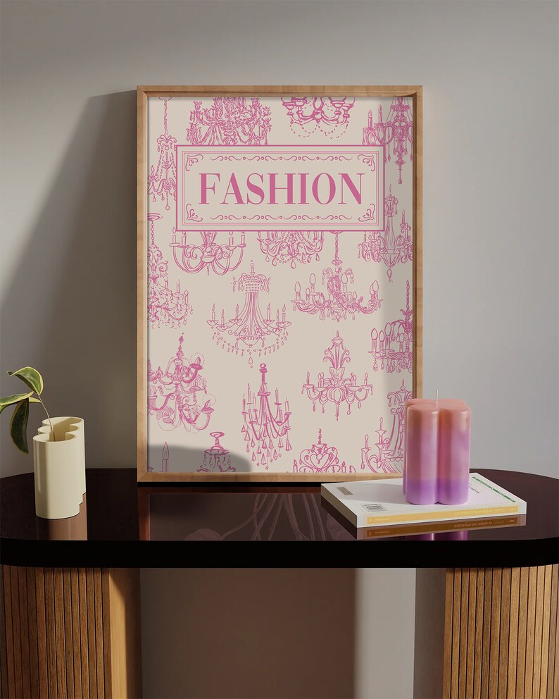 May include: A framed print with a white background and pink illustrations of chandeliers. The print has the word "FASHION" in pink letters in the centre.