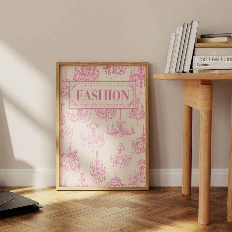 May include: A framed print with a cream background and a pink pattern of chandeliers. The word "FASHION" is written in pink in the centre of the print.