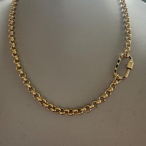 May include: A gold-colored chain necklace with a large, decorative clasp. The necklace is made of round, interlocking links. The clasp is a large oval shape with a screw closure.
