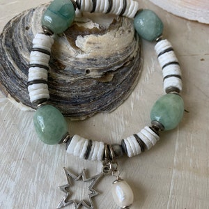Op de afbeelding: Een witte en groene kralen armband met een ster bedel en een parel hanger. De armband is gemaakt met witte schelp kralen en groene jade stenen.