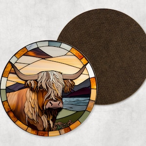 Może przedstawiać: Okrągła podkładka pod kubek z ilustracją krowy szkockiej w stylu witrażu na tle zachodu słońca. Podkładka ma brązowe filcowe podłoże.