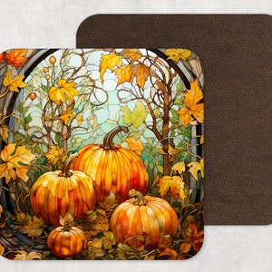 May include: A square coaster featuring a stained glass style illustration of three orange pumpkins surrounded by yellow and orange autumn leaves and vines. The coaster has rounded corners and a solid dark brown backing visible on the right side.