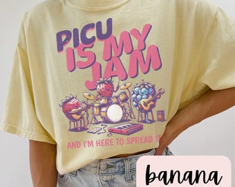 May include: A yellow t-shirt with the text "PICU IS MY JAM" in pink and purple letters. The text is surrounded by cartoon images of a strawberry, blueberry, and a banana playing musical instruments. The text below the images reads "AND I'M HERE TO SPREAD IT".