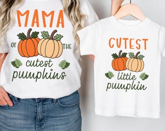 May include: Two white t-shirts with pumpkin graphics. One says "MAMA of the cutest pumpkins" and the other says "CUTEST little pumpkin". The pumpkins are orange and tan with green leaves. The shirts are on a hanger.