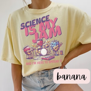 May include: A yellow t-shirt with a graphic of fruit playing instruments. The text on the shirt reads "Science is my jam and I'm here to spread it".