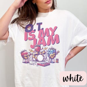 May include: White t-shirt with a graphic of fruit playing instruments. The text "O.T. is my jam" is printed in pink on the shirt.