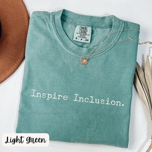 May include: Light green t-shirt with the text "Inspire Inclusion." printed in white. The shirt is made of a soft, comfortable material.