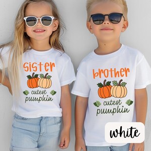 May include: Two children wearing white t-shirts with orange text and pumpkin graphics. One shirt says "Sister" and the other says "Brother". Both shirts have the text "cutest pumpkin".