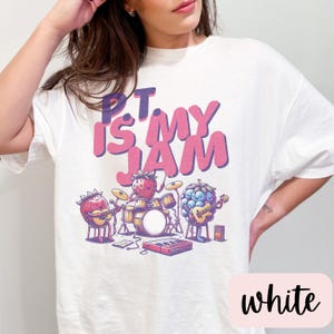 May include: White t-shirt with a pink and purple graphic of fruit playing instruments. The text "PT is my JAM" is printed on the shirt.