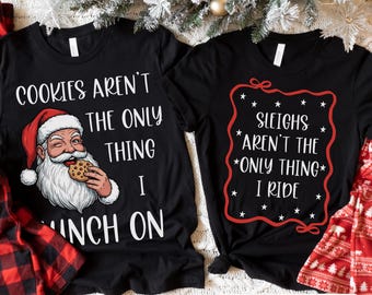 Può includere: Due magliette nere con testo a tema natalizio. Una maglietta presenta Babbo Natale che mangia un biscotto con la scritta "COOKIES AREN'T THE ONLY THING I INCH ON." L'altra maglietta dice "SLEIGHS AREN'T THE *ONLY THING* I RIDE."