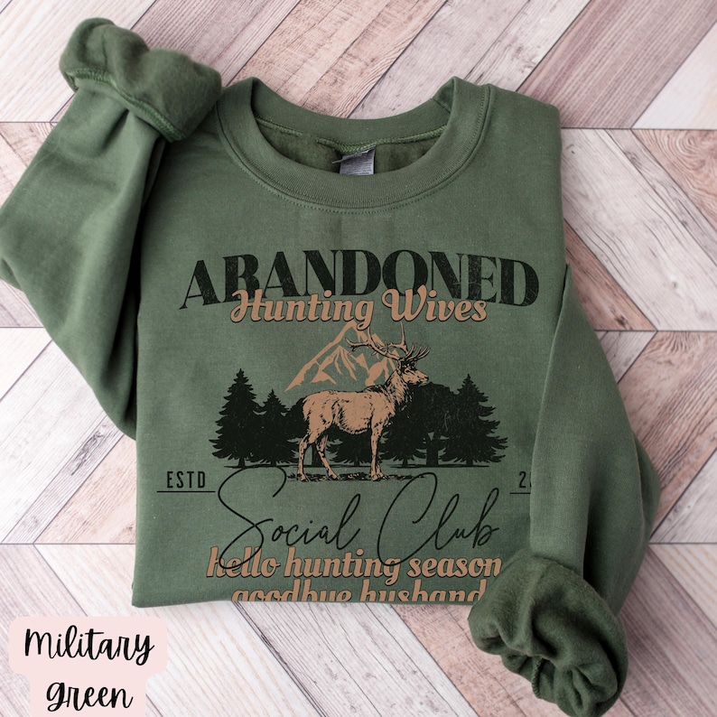 May include: A green sweatshirt with the text "Abandoned Hunting Wives Social Club" and a graphic of a deer in a forest. The text below the graphic says "Hello hunting season goodbye husband."