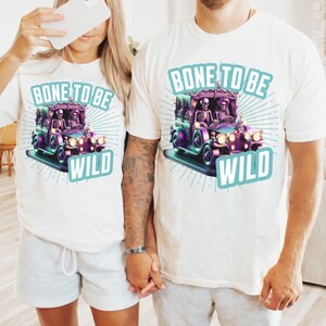 May include: Two white t-shirts with a graphic of skeletons driving a hearse. The text on the shirts reads "Bone to be Wild".