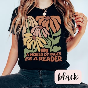 May include: Black t-shirt with a graphic of stylized flowers and the text "In a world of pages be a reader".