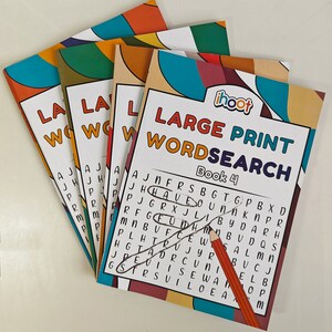 May include: Four "Large Print Wordsearch" puzzle books are fanned out, with the cover of the front book showing the text "Book 4". The covers have colorful geometric designs. A pencil is drawn on the puzzle page, circling words.