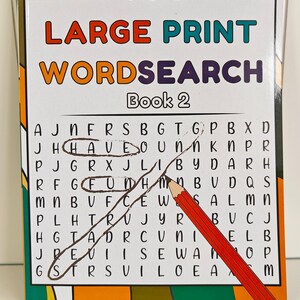 May include: A "Large Print Wordsearch Book 2" with a pencil and pen. The word search is in a grid with circled words. The book has a colorful cover with the brand "ihoot".