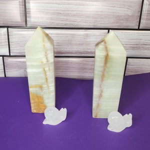 May include: Two white and green onyx crystal towers with a white snail figurine in front of each tower. The towers are on a purple surface.