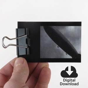 May include: A black and white photograph of a large airship, or dirigible, flying in the sky. The photo is attached to a black card with a binder clip. The text "Digital Download" is printed below the image.
