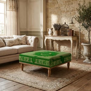 Può includere: Un pouf quadrato con rivestimento in tessuto verde brillante caratterizzato da un dettagliato motivo floreale e geometrico. Il mobile è sostenuto da quattro gambe in legno chiaro dal design tornito, che offrono una base stabile alla seduta.