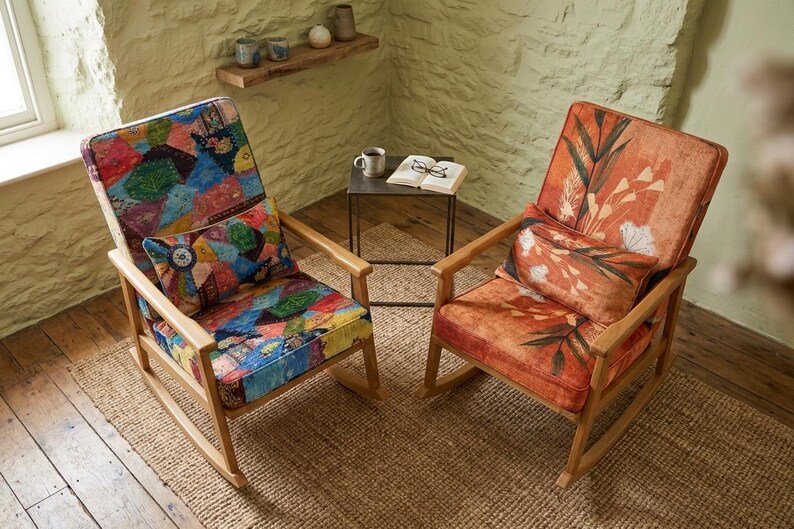 May include: Two wooden rocking chairs with patterned upholstery. One chair has a colourful patchwork design, the other an orange floral pattern. Both chairs have matching cushions and are set on a woven rug.