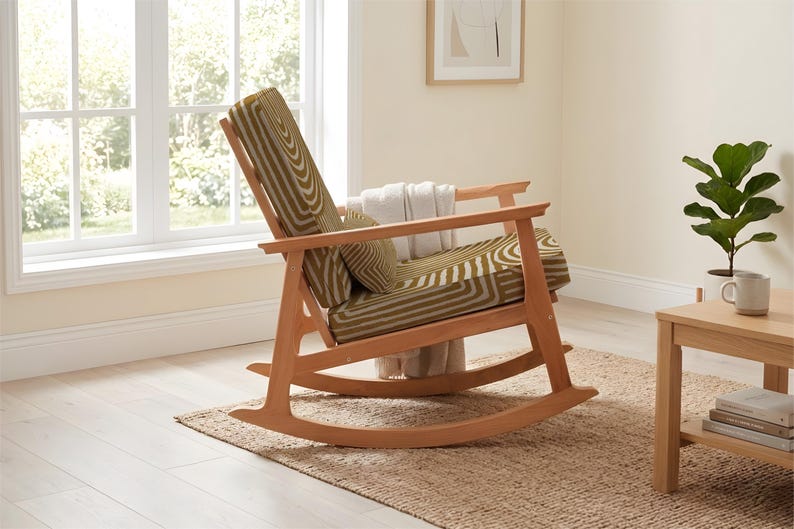 May include: A wooden rocking chair with a green and white geometric patterned cushion. The chair is in a bright room with a window, a small side table, and a plant. The chair has a classic design and is made of light-colored wood.
