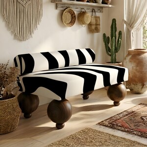 May include: A backless bench featuring a thick, cylindrical cushion upholstered in a bold black and white zebra-stripe pattern. The seat is supported by four large, dark brown wooden spherical legs, each resting on a smaller, flat circular base.