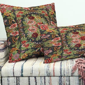 May include: Two decorative cushions with a floral pattern in shades of red, pink, yellow, and green on a dark background. The cushions are rectangular and square-shaped, resting on a striped sofa. The floral design is reminiscent of a tapestry.