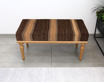May include: A rectangular ottoman with a brown and beige striped upholstered top. The ottoman has four turned wooden legs and a light brown frame. The design is simple and the colours are neutral, suitable for various interior styles.