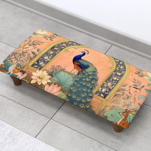 May include: A rectangular footstool with a decorative peacock design. The stool features a peach-colored background with a peacock, lotus flowers, and a deer. The legs are made of wood.