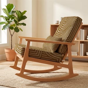 May include: A wooden rocking chair with a light brown frame and olive green and white patterned upholstery. The chair is set on a beige rug. A potted plant and a wooden shelf are visible in the background. The chair's design is modern.