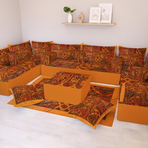 Puede incluir: Un juego de sala modular con una paleta de colores cálidos. El conjunto incluye un sofá esquinero, una mesa de centro y una alfombra, todos con una tela estampada en tonos naranja, rojo y dorado. Los muebles están sobre un suelo claro.