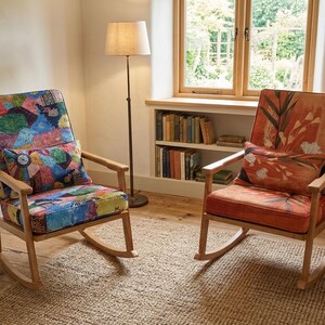 May include: Two wooden rocking chairs with patterned cushions. One chair features a patchwork design, the other an orange floral pattern. A floor lamp and a small side table are also visible. The chairs are in a room with a window.